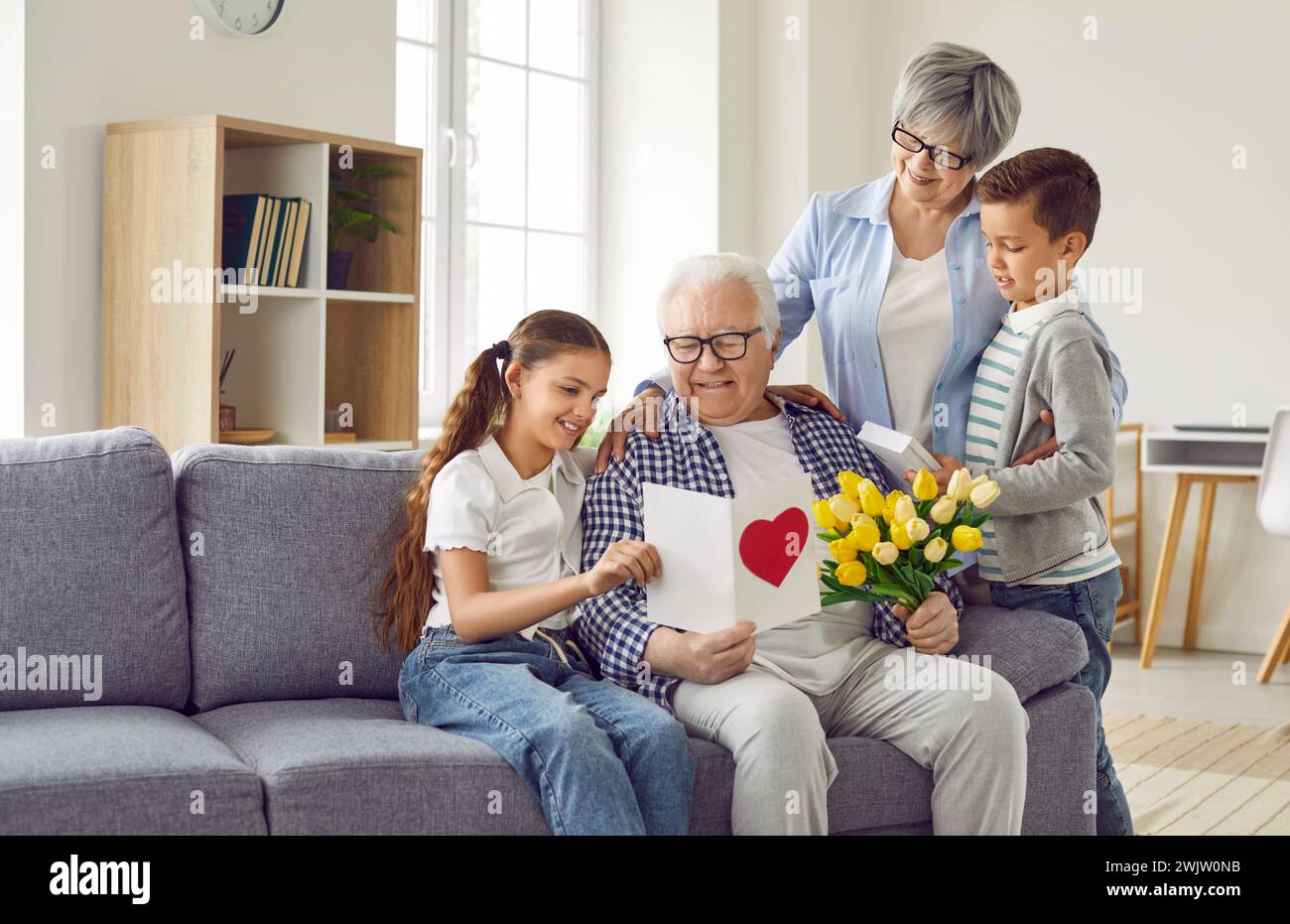 Happy grandfather receives a greeting card and a bouquet of flowers from his family Stock Photo