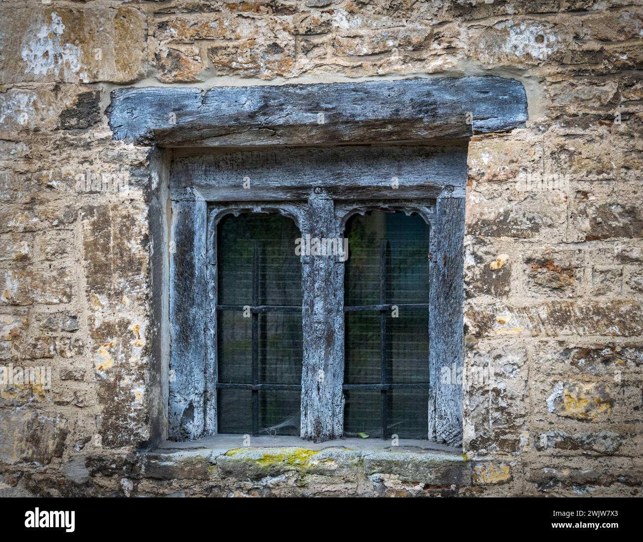 A very old window. The frame is unpainted hardwood with inner metal supports  and wire mesh Stock Photo