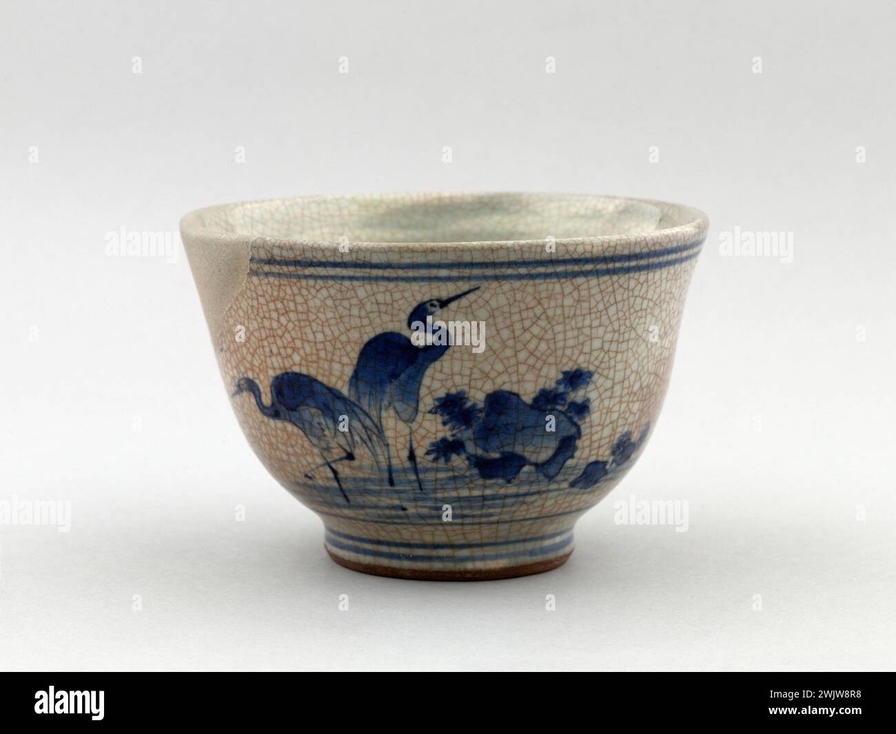 Tea bowl decorated with herons and cascade. Japan, province of Hizen, between 1650 and 1680. Ceramic. Paris, Cernuschi museum. On the outer side, patterns painted blue of herons and waterfalls. Above and at the base, two horizontal lines go around. BLEU, BOL A THE, Blue, CERAMIQUE, CRACKLED, CRAQUELURE, Ceramic, DECOR, DECORATE, Heron, TEA BOWL, VAISSELLE, Water, Waterfall, cascade Stock Photo