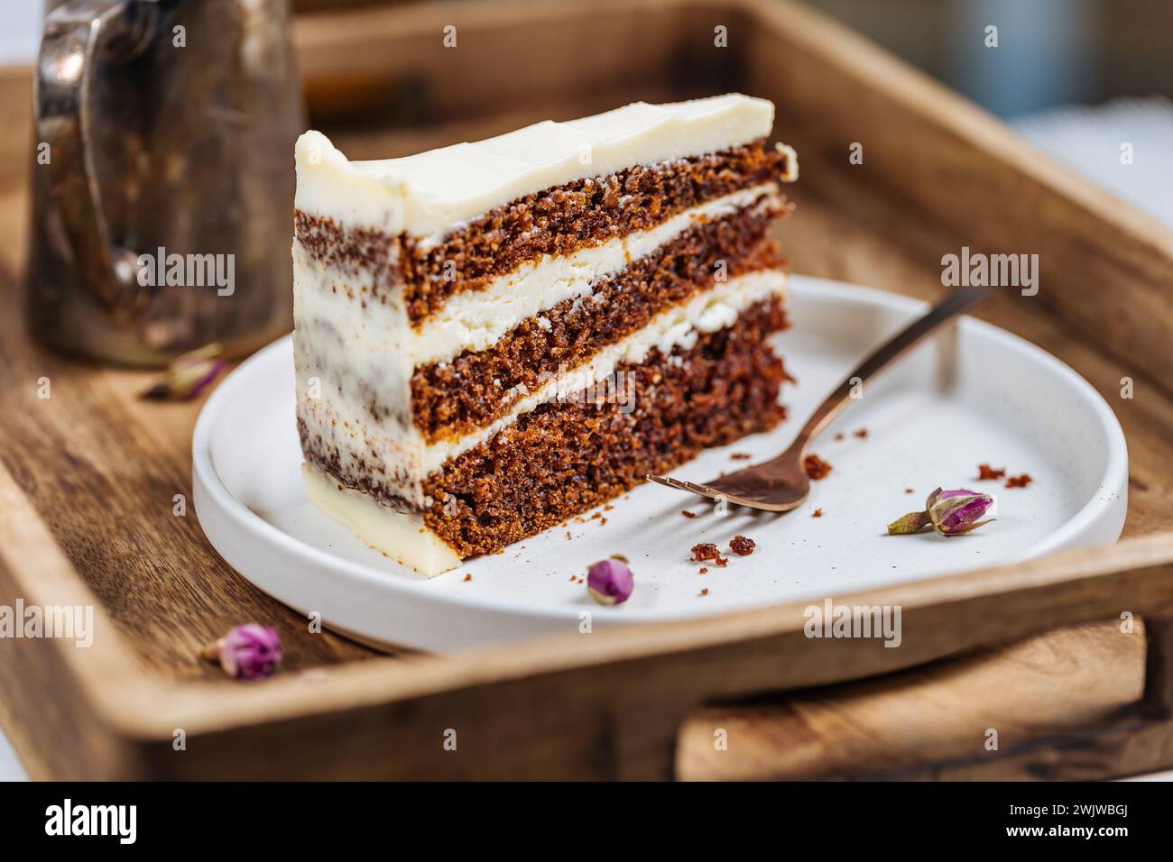 A piece of carrot cake served on rustic wooden tray. bright sunny scene. Layered cake with cream cheese frosting and fluffy biscuit. Stock Photo