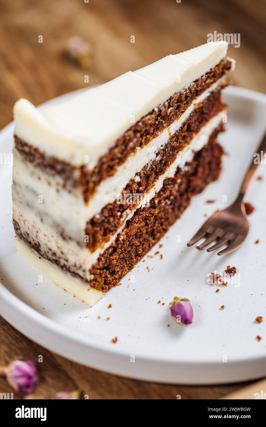 A piece of carrot cake served on rustic wooden tray. bright sunny scene. Layered cake with cream cheese frosting and fluffy biscuit. Stock Photo