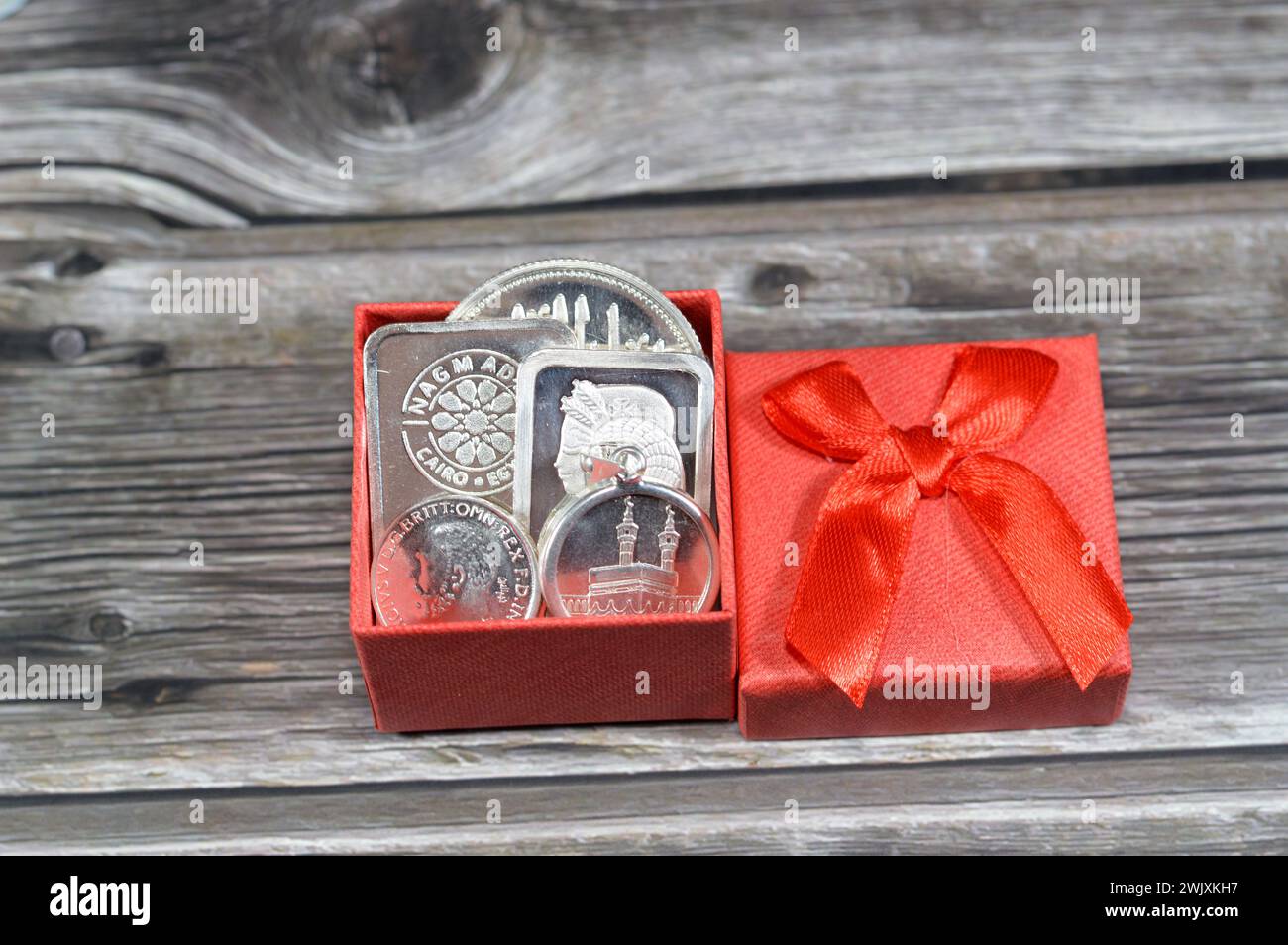 Cairo, Egypt, February 9 2024: A red small gift box with Nagm Ad-Din Silver bars and coins, pure precious silver metal of ounce, 50 grams bar, King Ge Stock Photo
