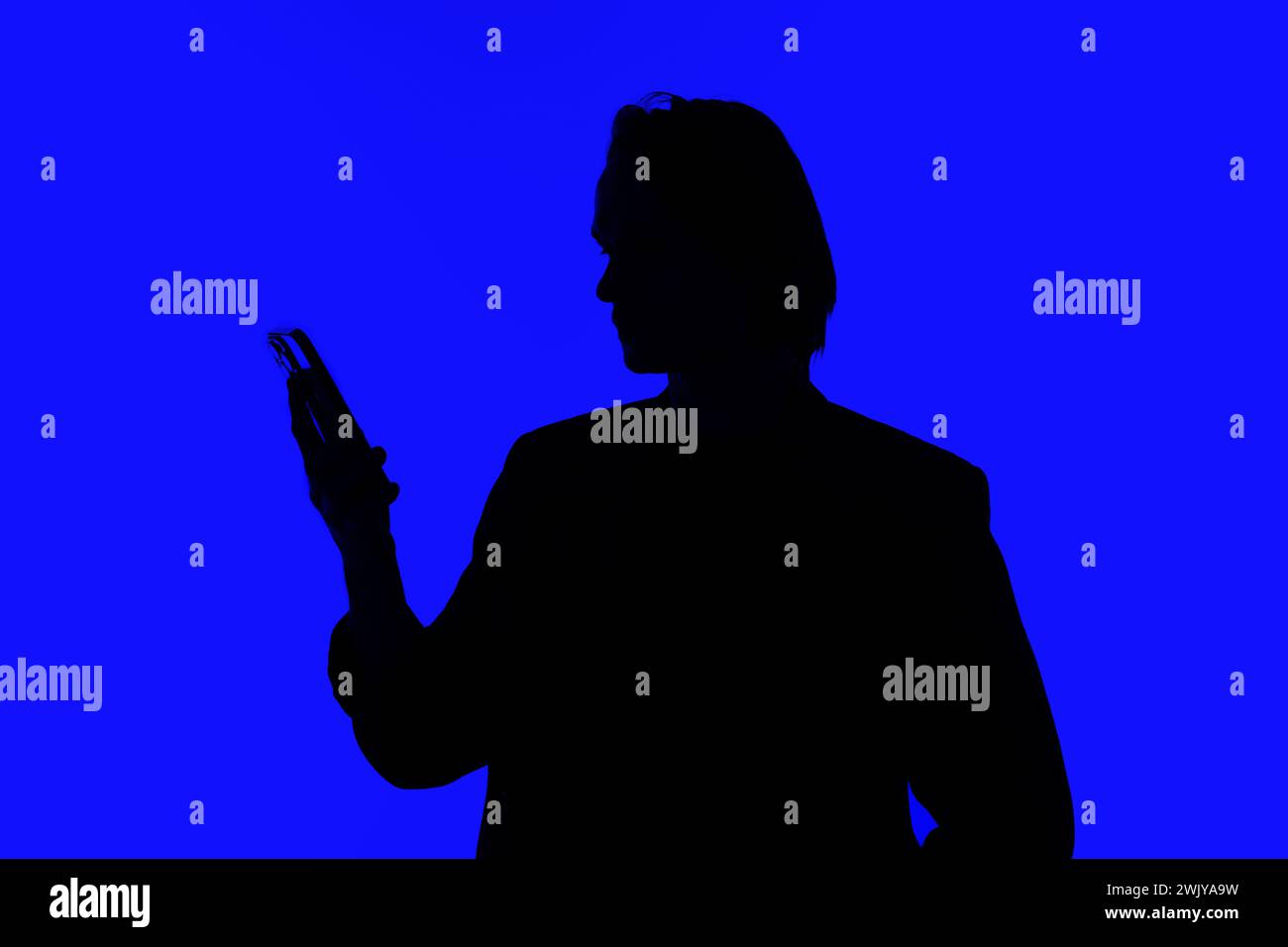 Silhouette an elegant businessman using a modern smartphone in a jacket standing on a blue glowing background, a futuristic concept Stock Photo