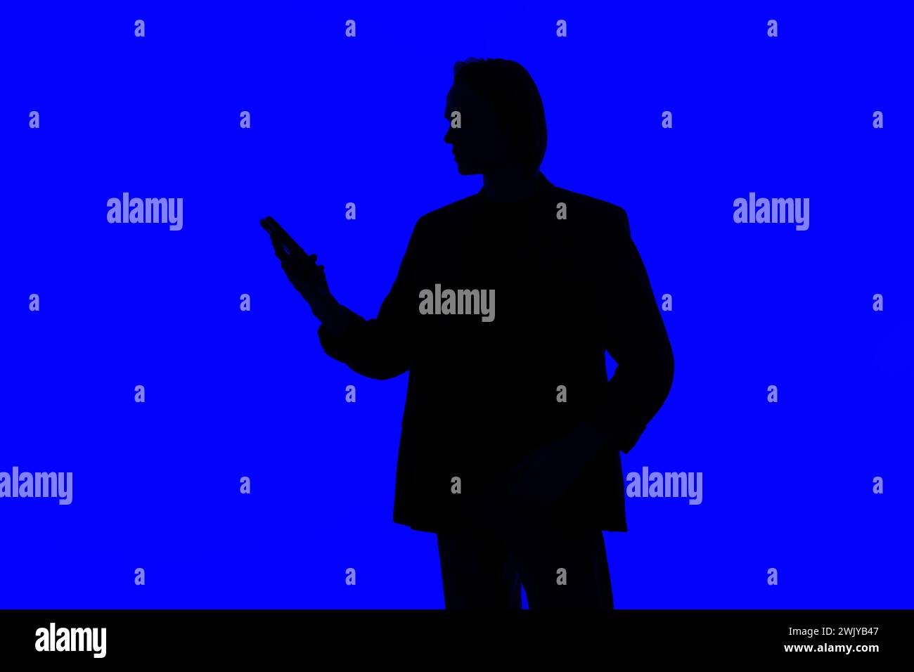 Silhouette an elegant businessman using a modern smartphone in a jacket standing on a blue glowing background, a futuristic concept Stock Photo