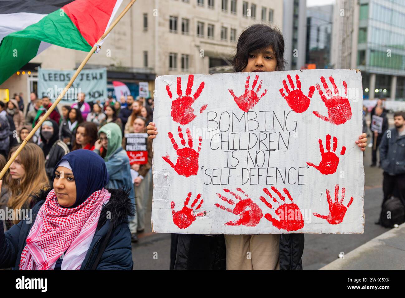 Leeds, UK. 17 FEB, 2024. A young child at the pro palestine protest in Leeds city square holds a sign with bloodied handprints and reads 'Bombing Children is not self-defence' . Credit Milo Chandler/Alamy Live News Stock Photo