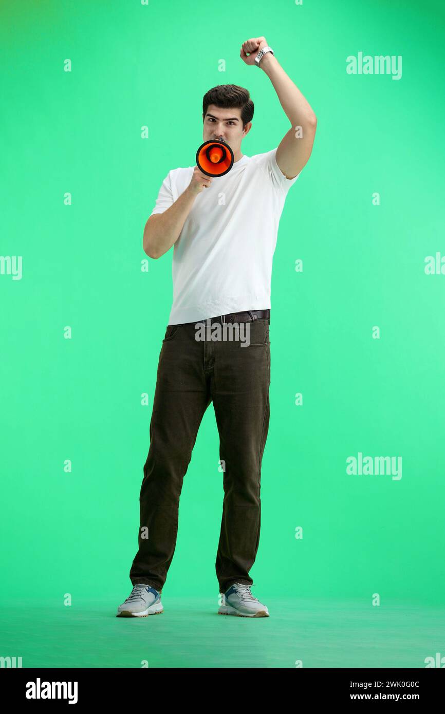 A man in full height, on a green background, with a megaphone Stock Photo