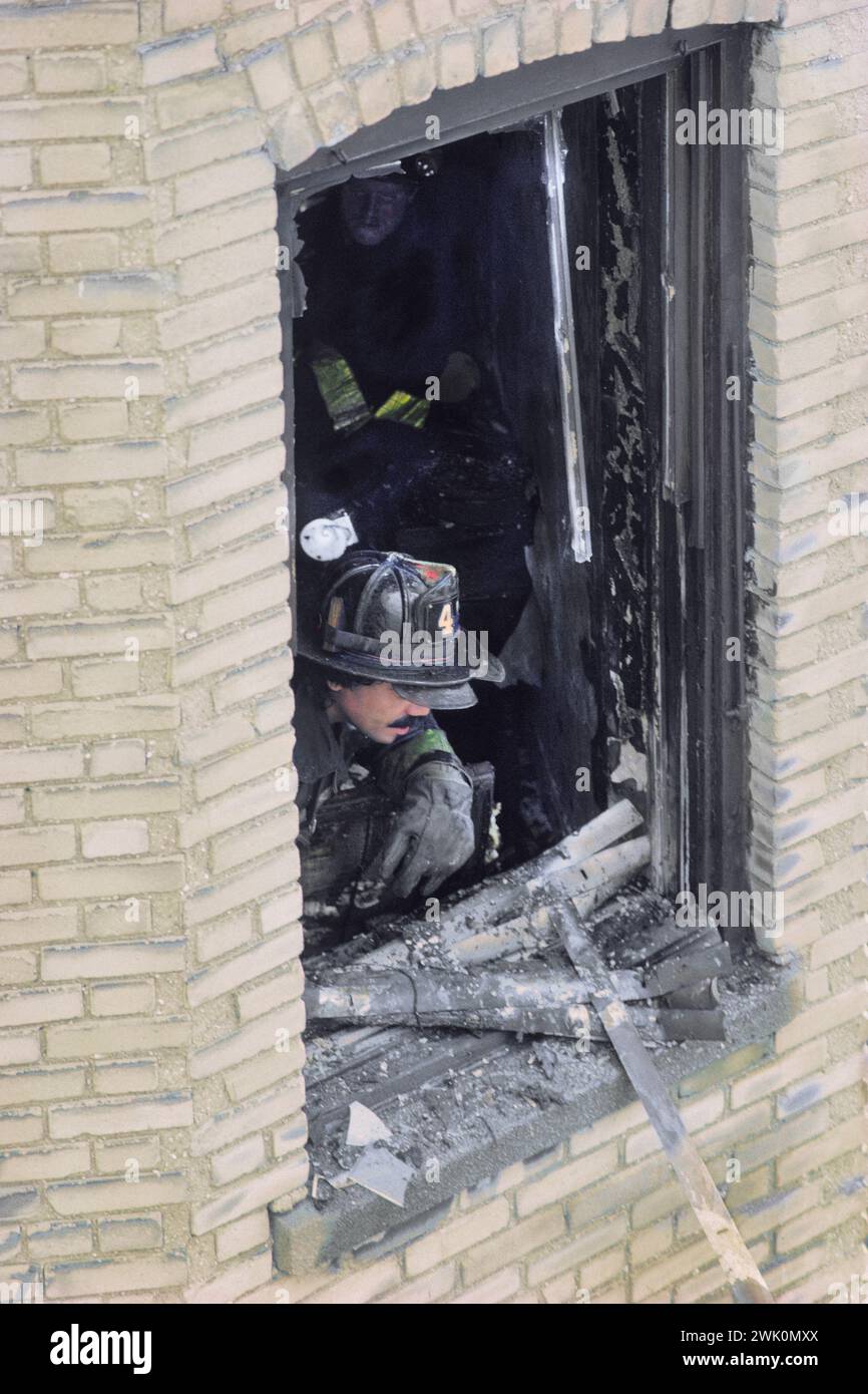 Fireman or firefighter surveying damage from a building window with broken glass. Fire scene The Bronx, New York City USA Stock Photo