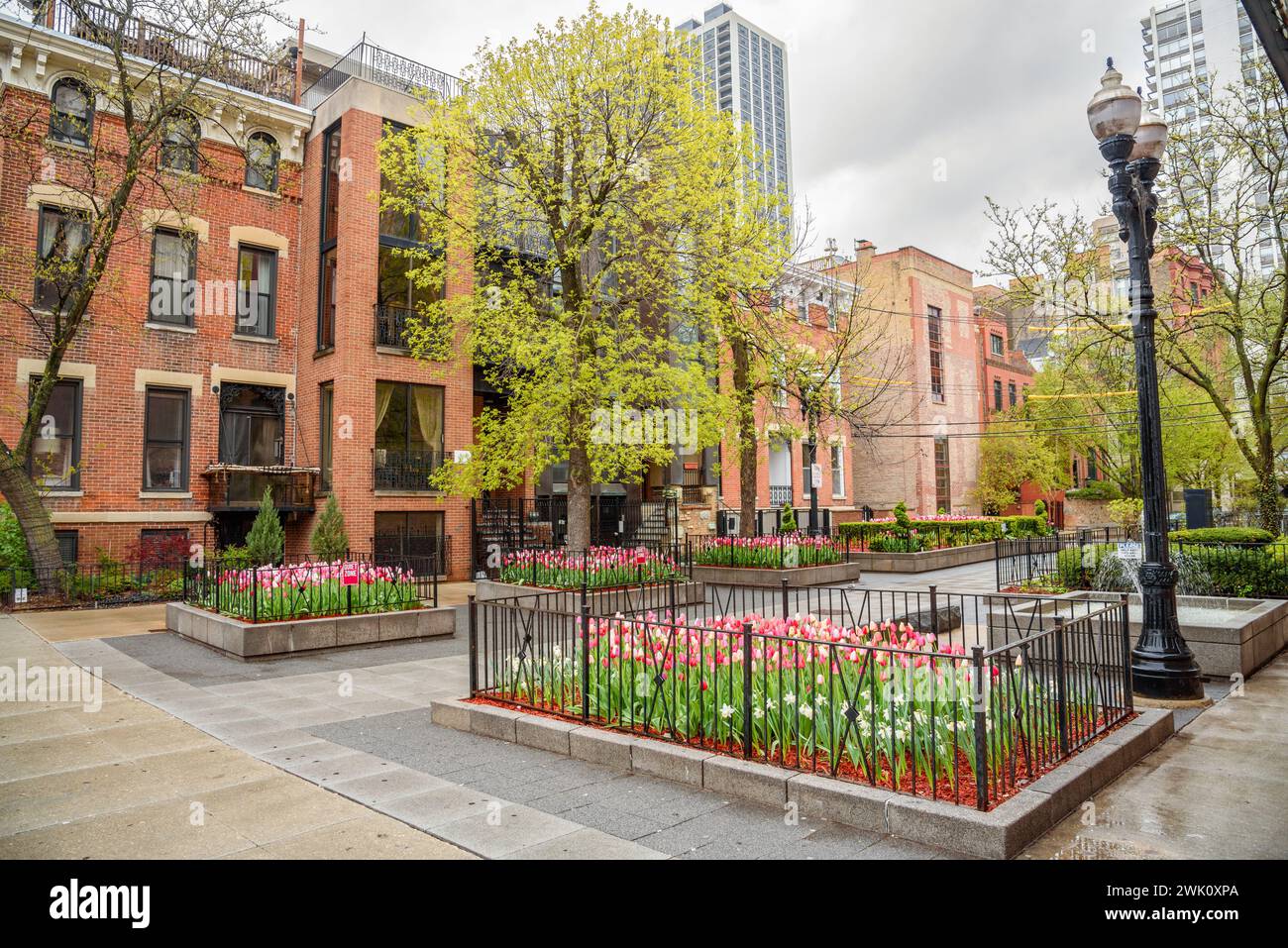 Small square with flower beds and a fountain surrounded by brick residentail buildings in old town Chicago on a cloudy spring day Stock Photo