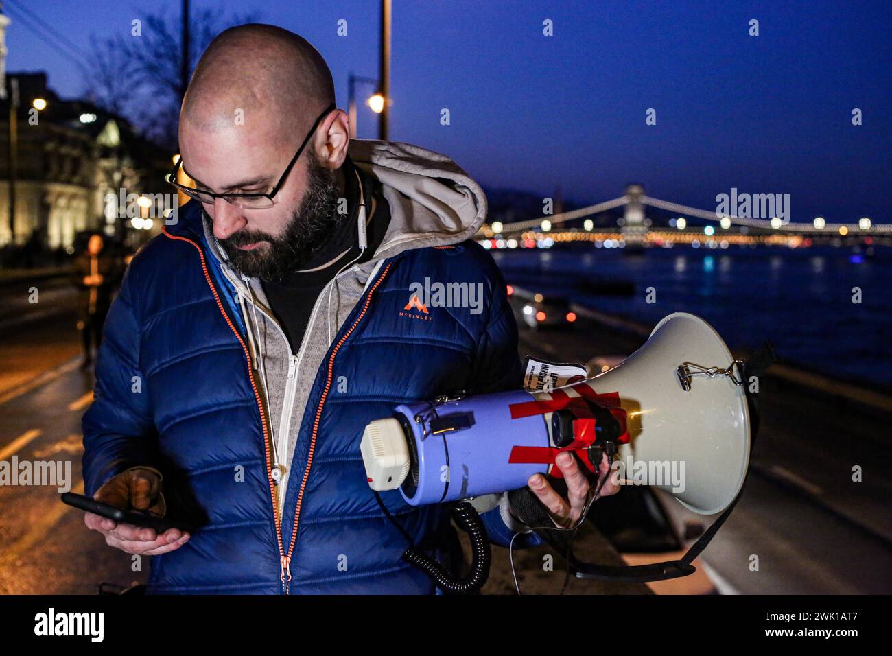 Budapest, Budapest, Hungary. 17th Feb, 2024. Hungarian activist, Balasz T., holds a bull horn with the chain bridge in back ground along the Danube after a speech where Hungarian Prime Minister VIKTOR ORBAN made his annual speech and comments on three resignations of Hungarian President, KATALIN NOVAK; former Minister and leadership of Hungarian Reform Church, ZOLTAN BALOG and former Justice Minister, JUDIT VARGA following exposure of a man pardoned last year from covering up pedophilia in a children's home. The reveal has caused embarrassment and tarnished the image of Hungary's safe z Stock Photo