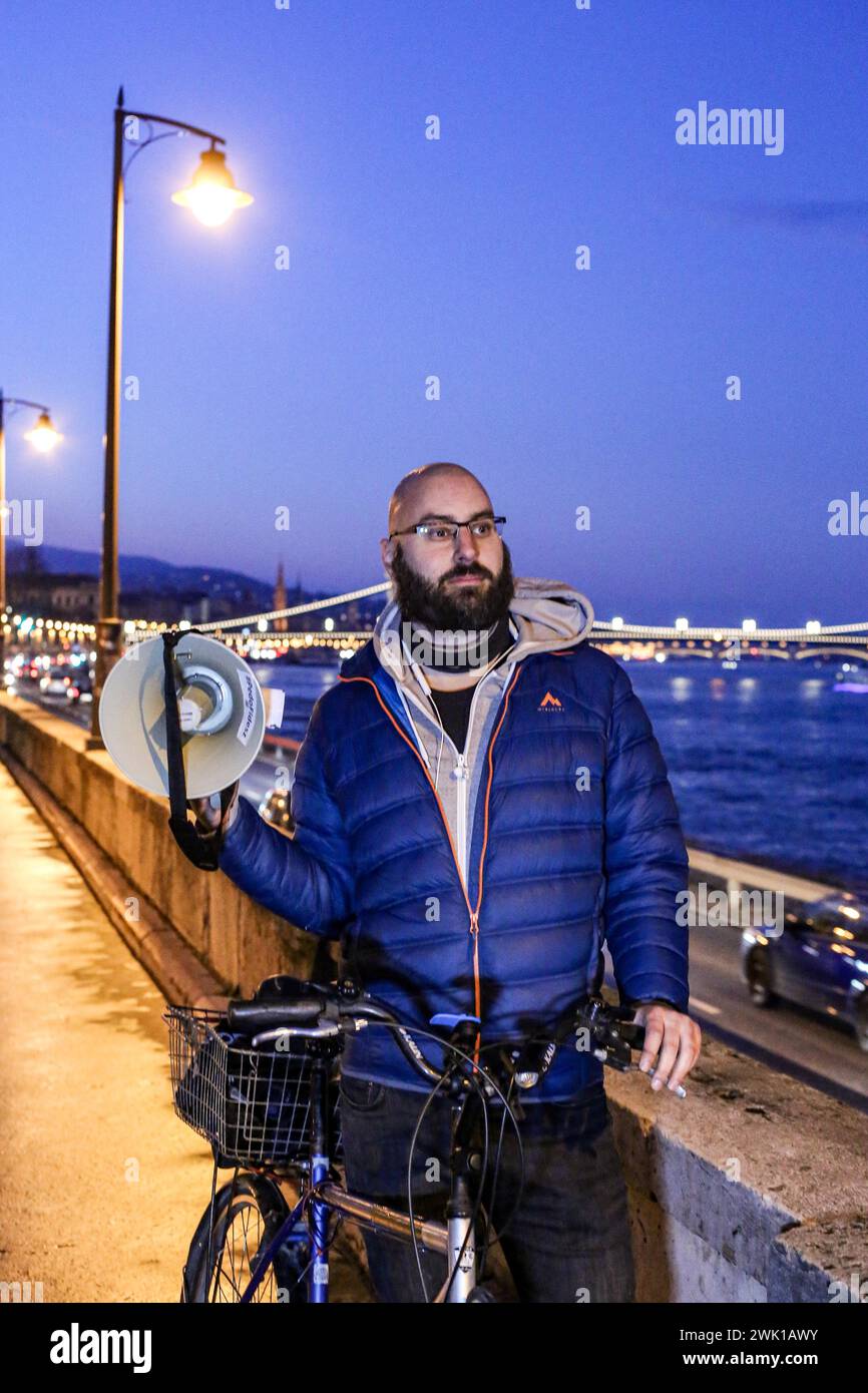 Budapest, Budapest, Hungary. 17th Feb, 2024. Hungarian activist, Balasz T., holds a bull horn with the chain bridge in back ground along the Danube after a speech where Hungarian Prime Minister VIKTOR ORBAN made his annual speech and comments on three resignations of Hungarian President, KATALIN NOVAK; former Minister and leadership of Hungarian Reform Church, ZOLTAN BALOG and former Justice Minister, JUDIT VARGA following exposure of a man pardoned last year from covering up pedophilia in a children's home. The reveal has caused embarrassment and tarnished the image of Hungary's safe z Stock Photo