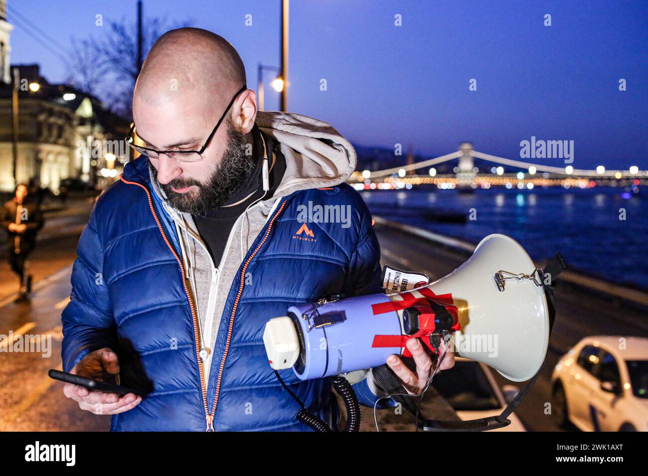 Budapest, Budapest, Hungary. 17th Feb, 2024. Hungarian activist, Balasz T., holds a bull horn with the chain bridge in back ground along the Danube after a speech where Hungarian Prime Minister VIKTOR ORBAN made his annual speech and comments on three resignations of Hungarian President, KATALIN NOVAK; former Minister and leadership of Hungarian Reform Church, ZOLTAN BALOG and former Justice Minister, JUDIT VARGA following exposure of a man pardoned last year from covering up pedophilia in a children's home. The reveal has caused embarrassment and tarnished the image of Hungary's safe z Stock Photo