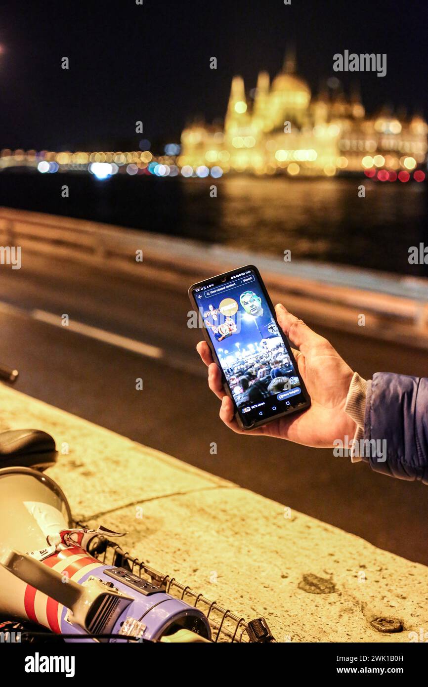 Budapest, Budapest, Hungary. 17th Feb, 2024. Hungarian activist, Balasz T., holds a phone demonstrating efforts by other activists and influencers the day after a massive protest took place in the capital towards Hungarian Prime Minister VIKTOR ORBAN and on the three resignations of Hungarian President, KATALIN NOVAK; former Minister and leadership of Hungarian Reform Church, ZOLTAN BALOG and former Justice Minister, JUDIT VARGA following exposure of a man pardoned last year from covering up pedophilia in a children's home. The reveal has caused embarrassment and tarnished the image of Hu Stock Photo