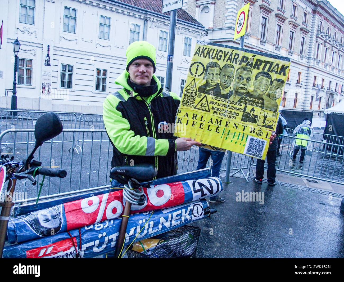 Budapest, Budapest, Hungary. 17th Feb, 2024. A Hungarian activist with his bike, holds sign saying Battery Party in protest of battery manufacturing as well as Throw Them from Parliament, in front of Varkert, where Hungarian Prime Minister VIKTOR ORBAN made his annual speech and comments on three resignations of Hungarian President, KATALIN NOVAK; former Minister and leadership of Hungarian Reform Church, ZOLTAN BALOG and former Justice Minister, JUDIT VARGA following exposure of a man pardoned last year from covering up pedophilia in a children's home. The reveal has caused embarrassment Stock Photo