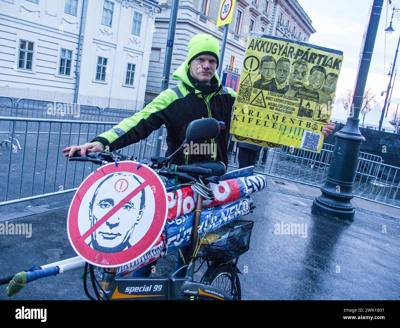 Budapest, Budapest, Hungary. 17th Feb, 2024. A Hungarian activist with his bike, holds sign saying Battery Party in protest of battery manufacturing as well as Throw Them from Parliament, in front of Varkert, where Hungarian Prime Minister VIKTOR ORBAN made his annual speech and comments on three resignations of Hungarian President, KATALIN NOVAK; former Minister and leadership of Hungarian Reform Church, ZOLTAN BALOG and former Justice Minister, JUDIT VARGA following exposure of a man pardoned last year from covering up pedophilia in a children's home. The reveal has caused embarrassment Stock Photo