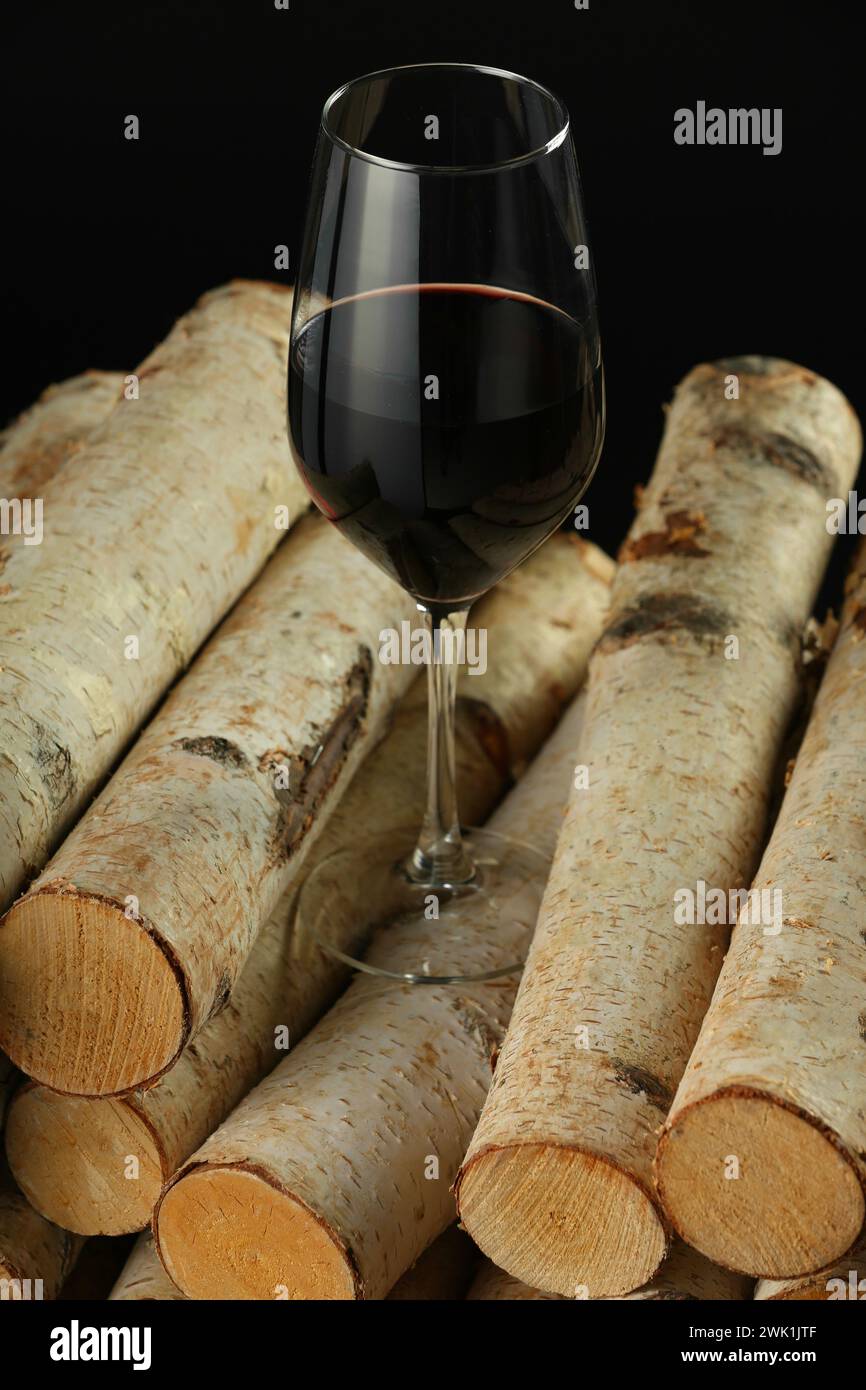 Red wine in wineglass on wooden logs against black background Stock Photo