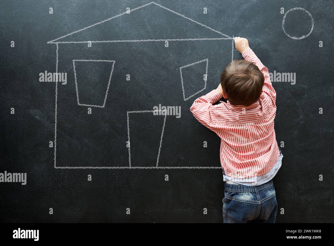 Kid, drawing and art of house on chalkboard of preschool as young student in classroom. Little boy, creative and imagination for sketch of home on Stock Photo