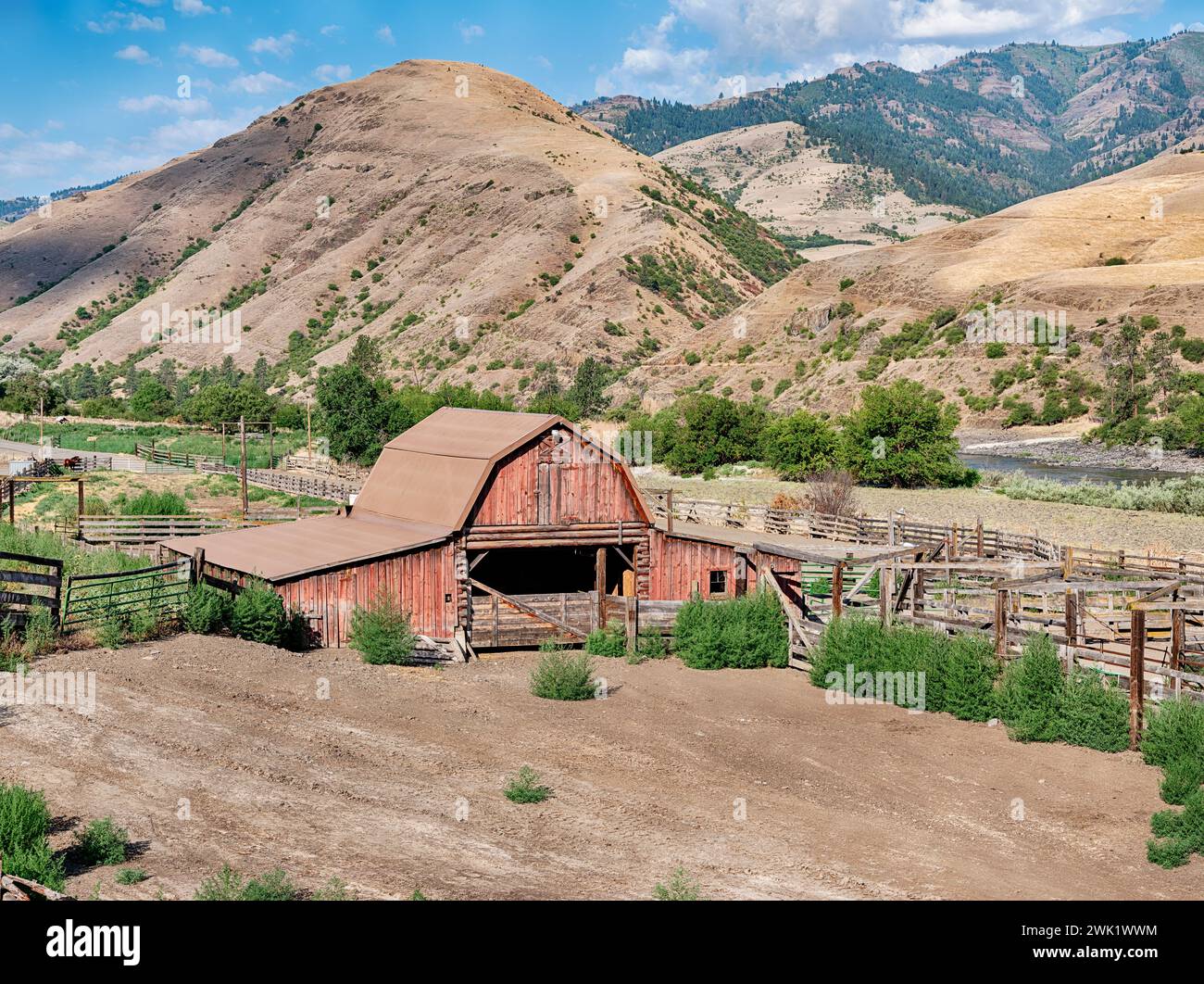 A rural ranch near Lucile, Idaho includes a classic red barn and wood corral next to the Lower Salmon River and mountains.. Stock Photo