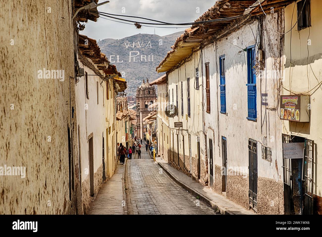 A narrow street leads downhill to the center of the city of Cusco while a sign on the distant mountain says Viva El Peru. Stock Photo