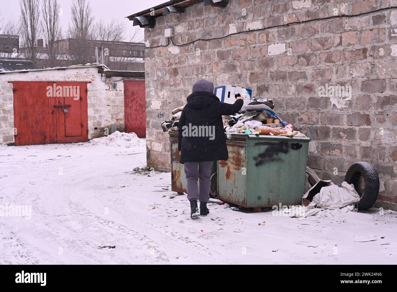 a woman throws unsorted garbage into an overflowing trash can Stock Photo