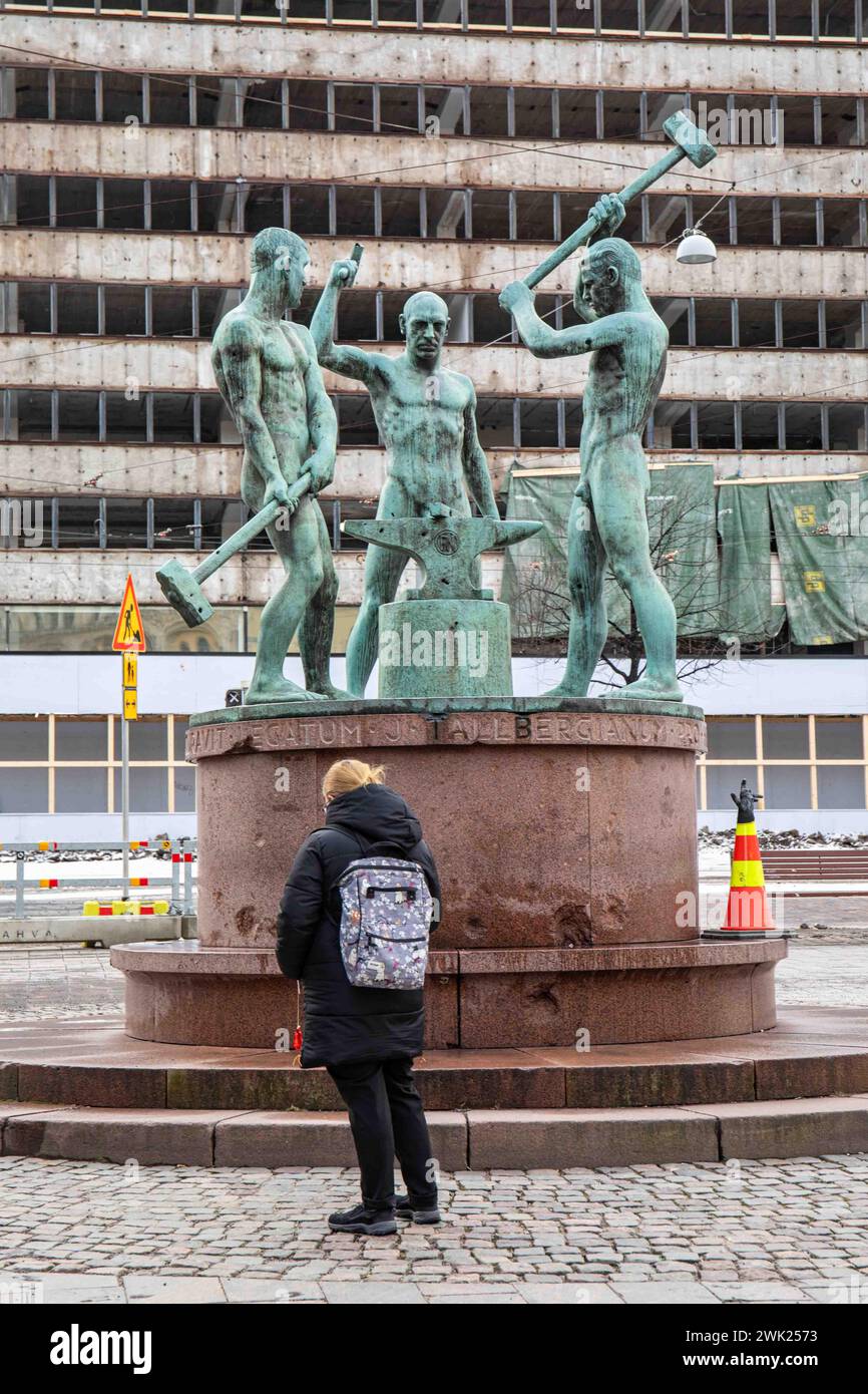 Woman with a backpack in front of Three Smiths Statue with office building under demolition in the background in Helsinki, Finland Stock Photo