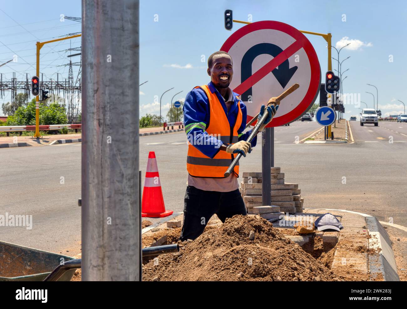 african american worker with a pickaxe digging a ditch in the highway to repair cabling on an isle at an intersection Stock Photo