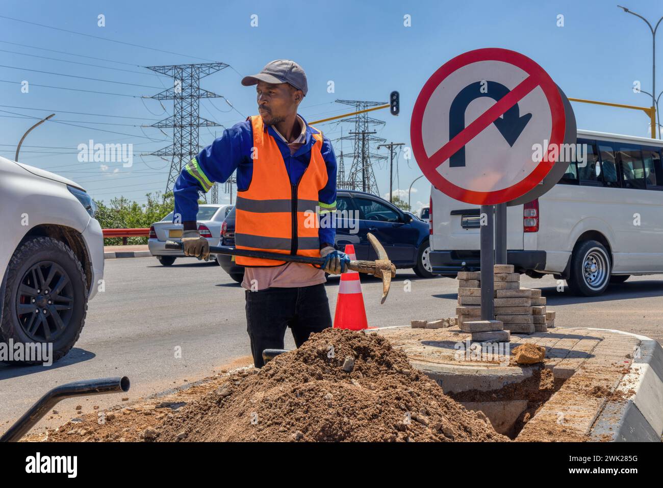 african american worker with a pickaxe digging a ditch in the highway to repair cabling on an isle at an intersection Stock Photo