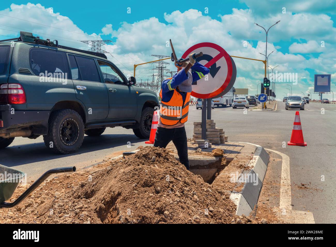 african american worker with a pickaxe digging a ditch in the highway to repair cabling on an isle at an intersection Stock Photo