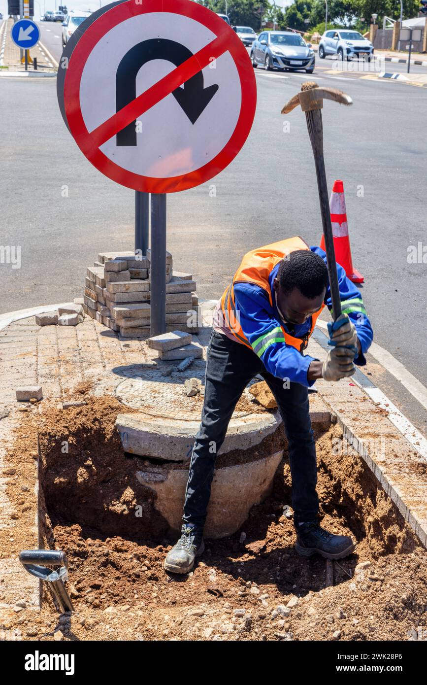 african american worker with a pickaxe digging a ditch in the highway to repair cabling on an isle at an intersection Stock Photo