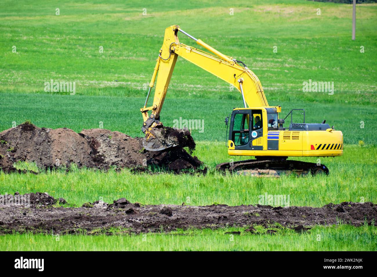 An excavator while digging a trench in a green field Stock Photo - Alamy
