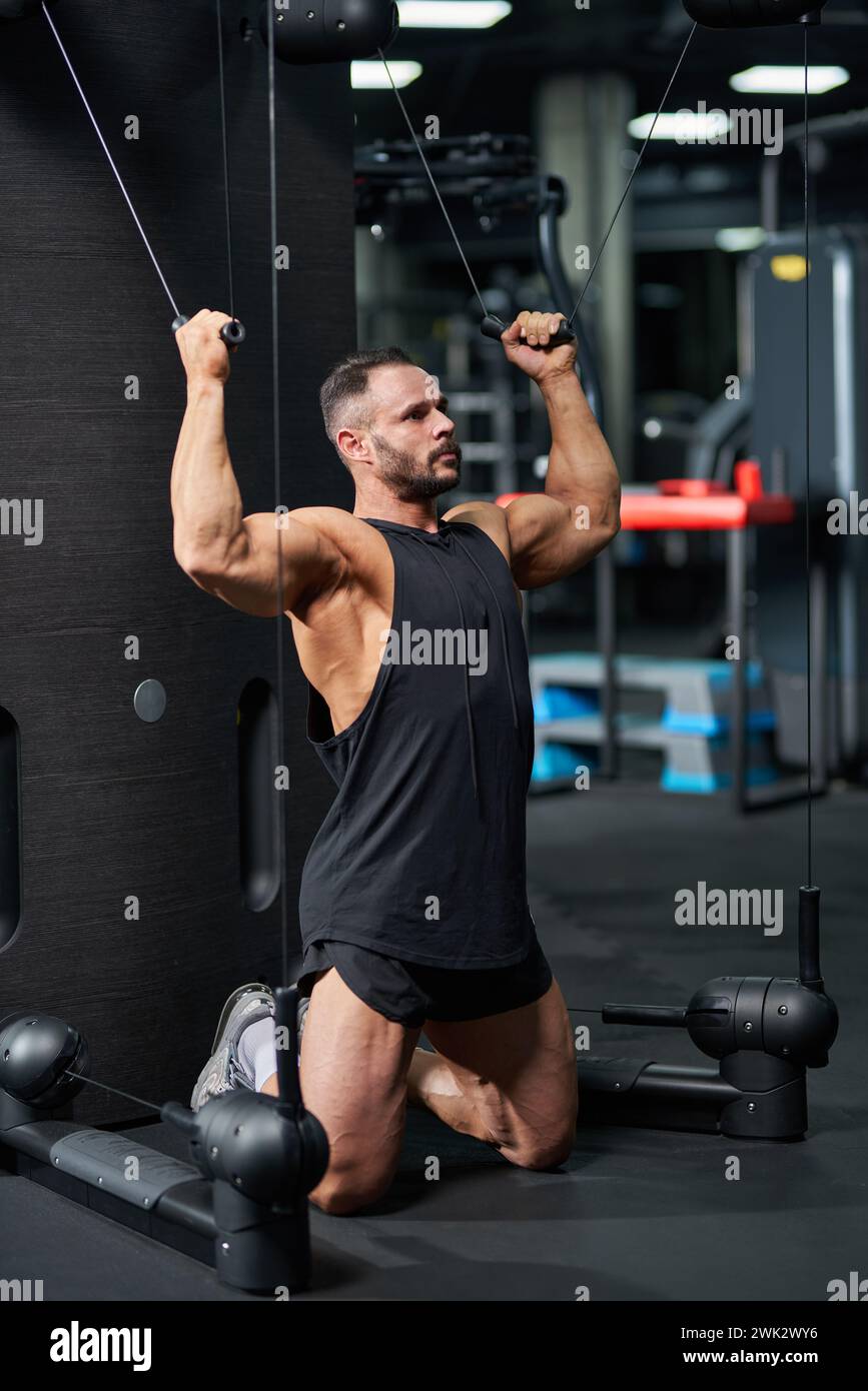 Serious sportsman wearing black tank top, doing exercise for biceps