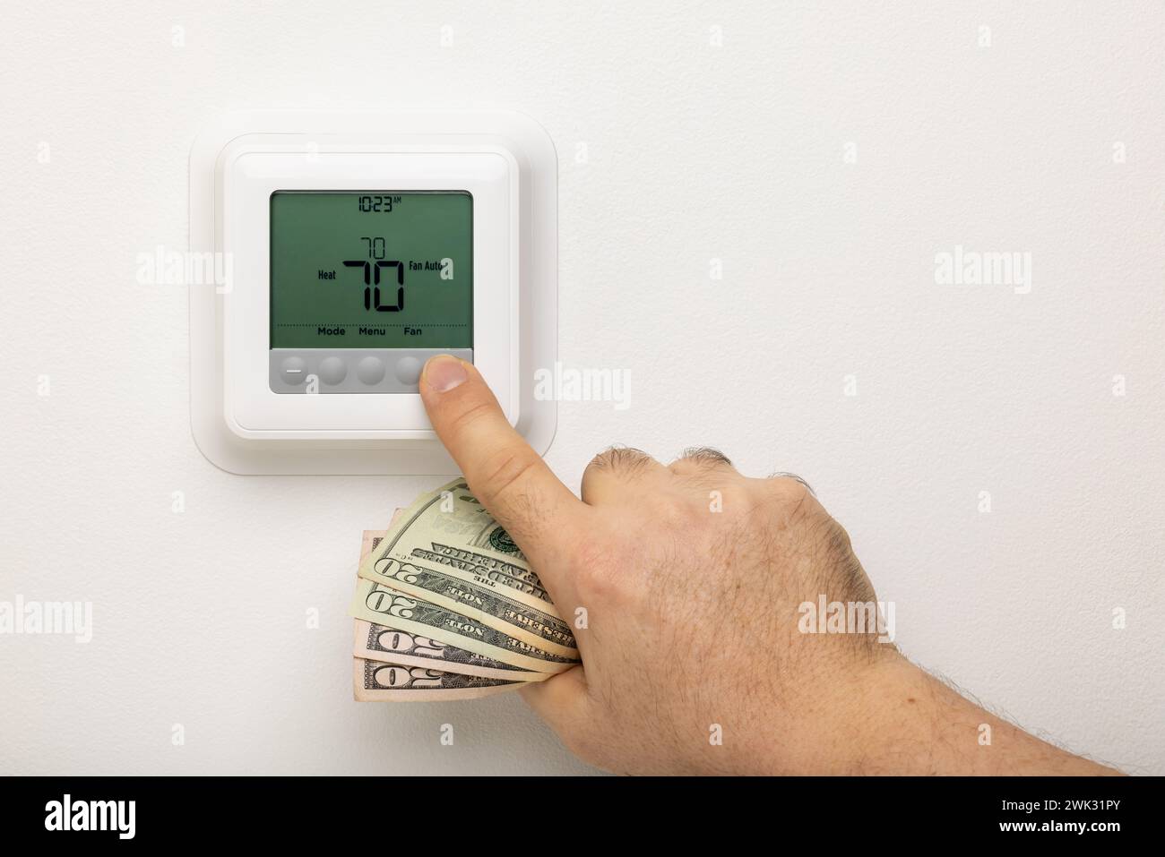 A hand holding money adjusting a thermostat. Stock Photo