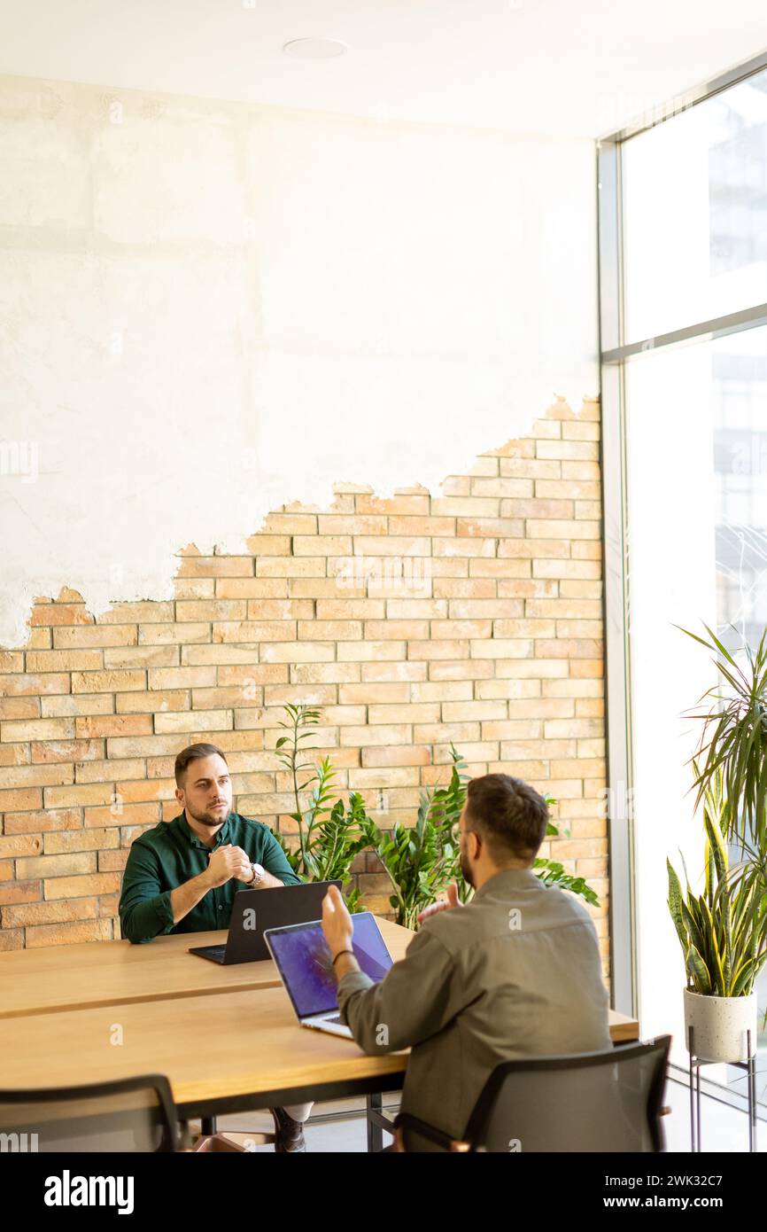 Two smiling professionals engage in a collaborative work session at a wooden table, their camaraderie evident in a contemporary office setting with an Stock Photo