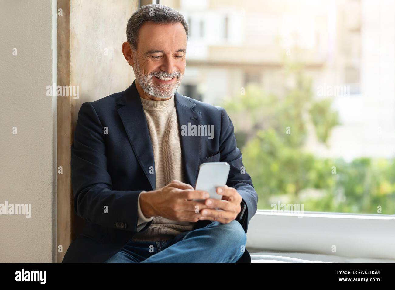 Smiling older man using a smartphone by the window Stock Photo