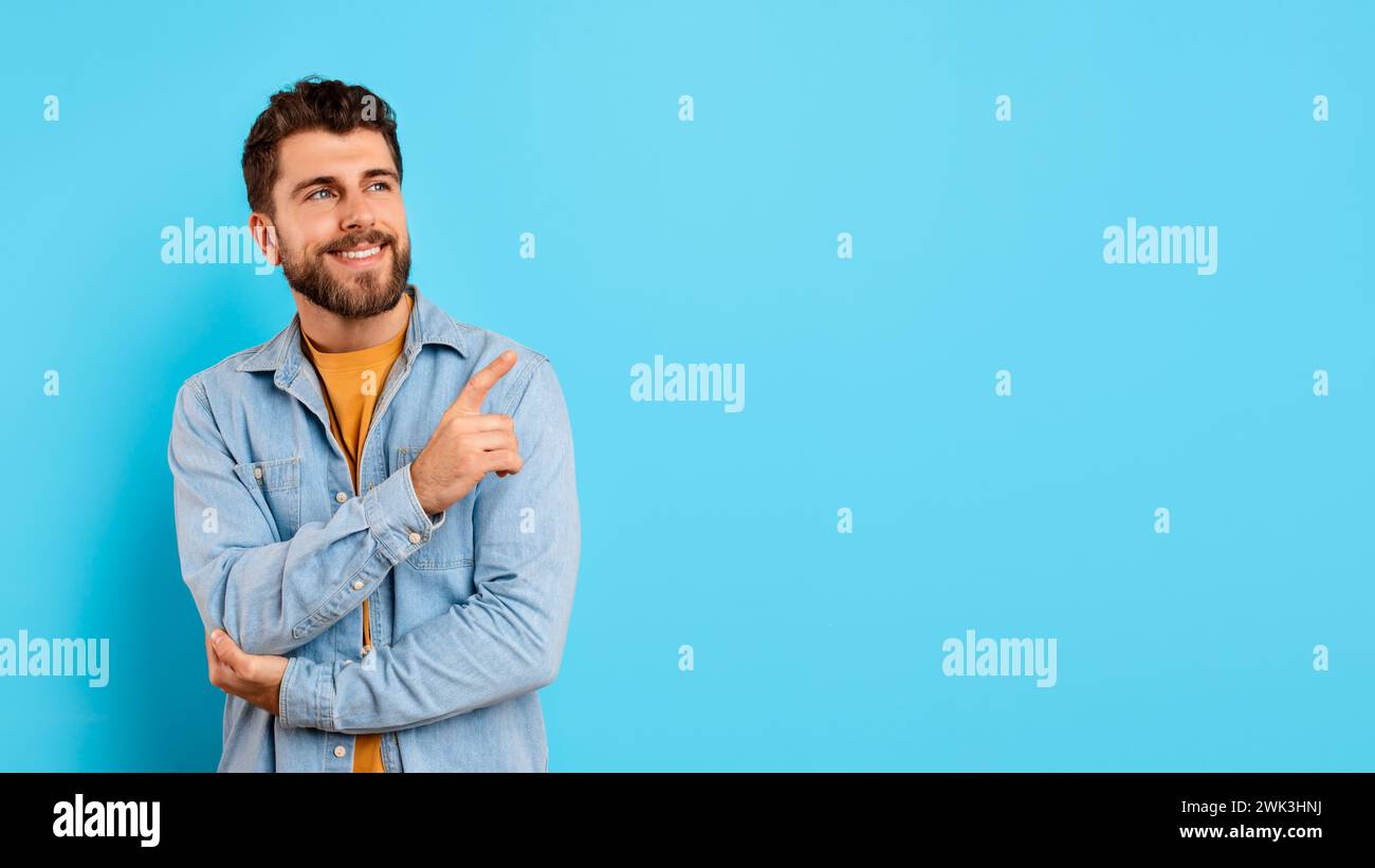 Smiling confident young man points aside on blue background, panorama Stock Photo
