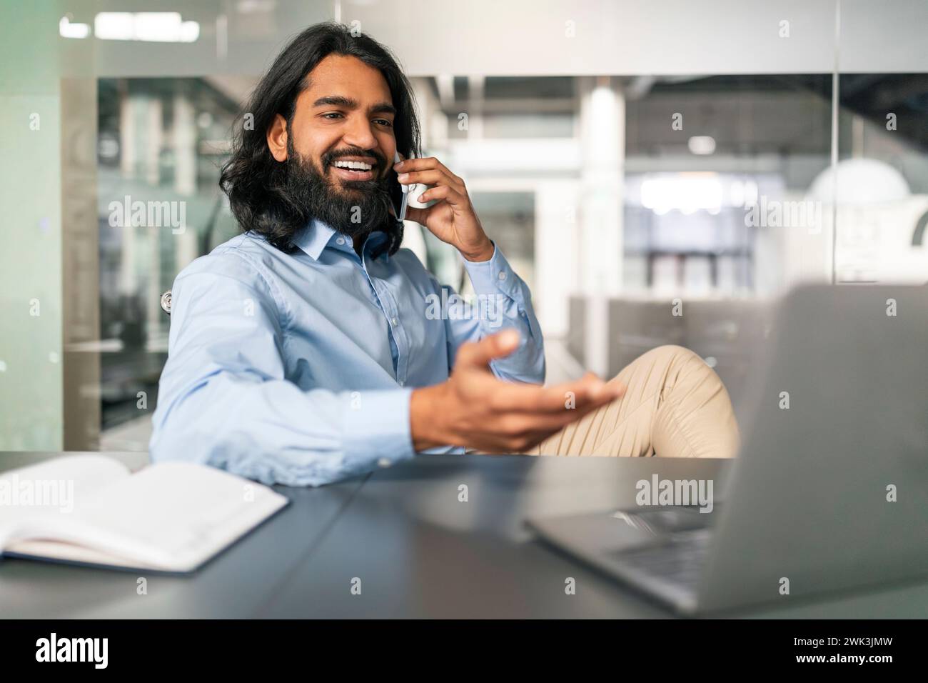 Indian Guy Talking On Cellphone Working On Computer At Office Stock Photo