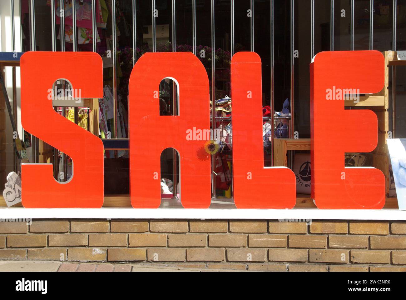 SALE sign spelled out in very large red eye catching block capital uppercase letters resting on brick wall outside part of small shop front window advertising a small one off retail business closing down in Essex England UK Stock Photo
