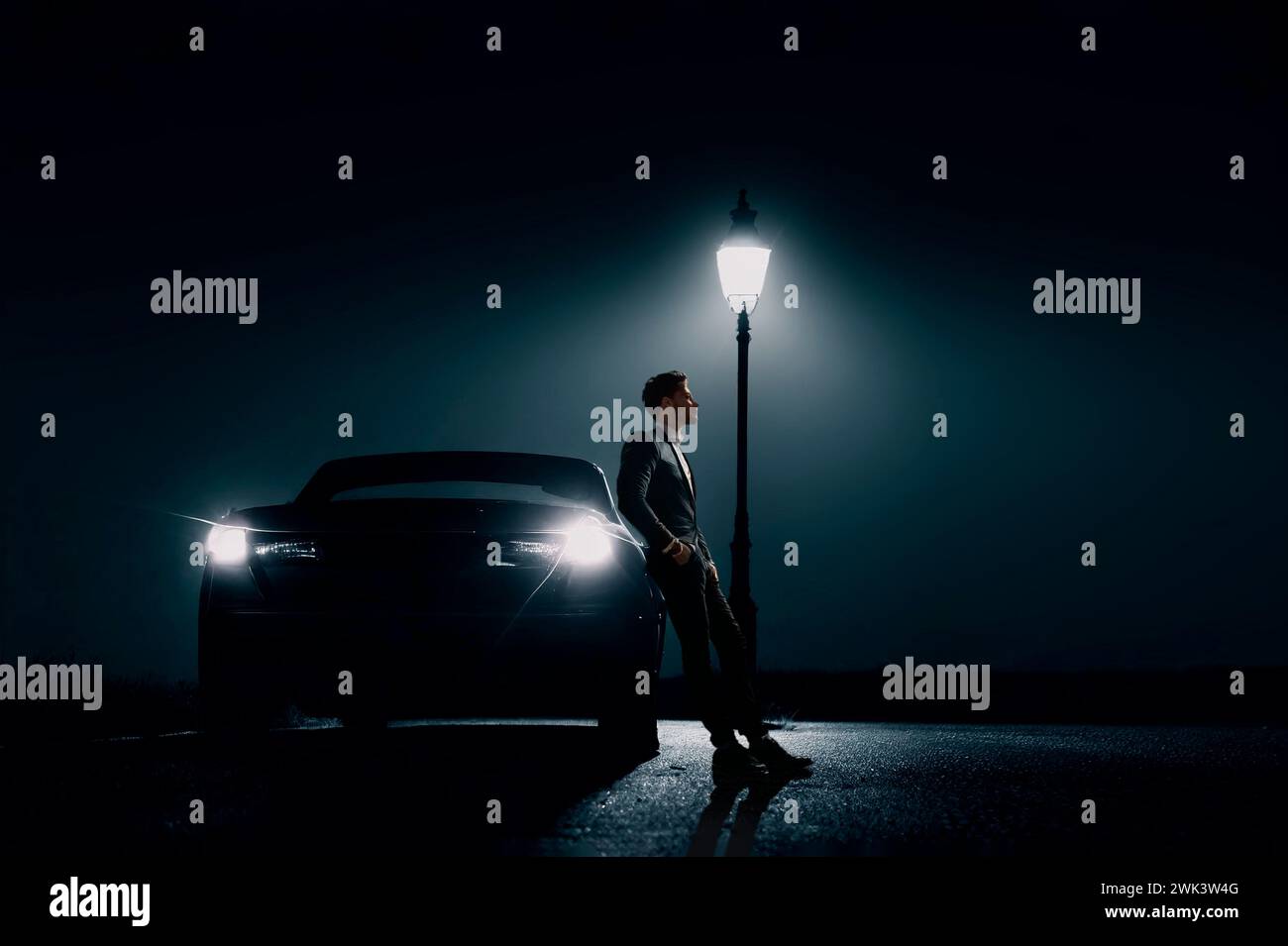 Man leaning against car with lamp post at night, USA Stock Photo