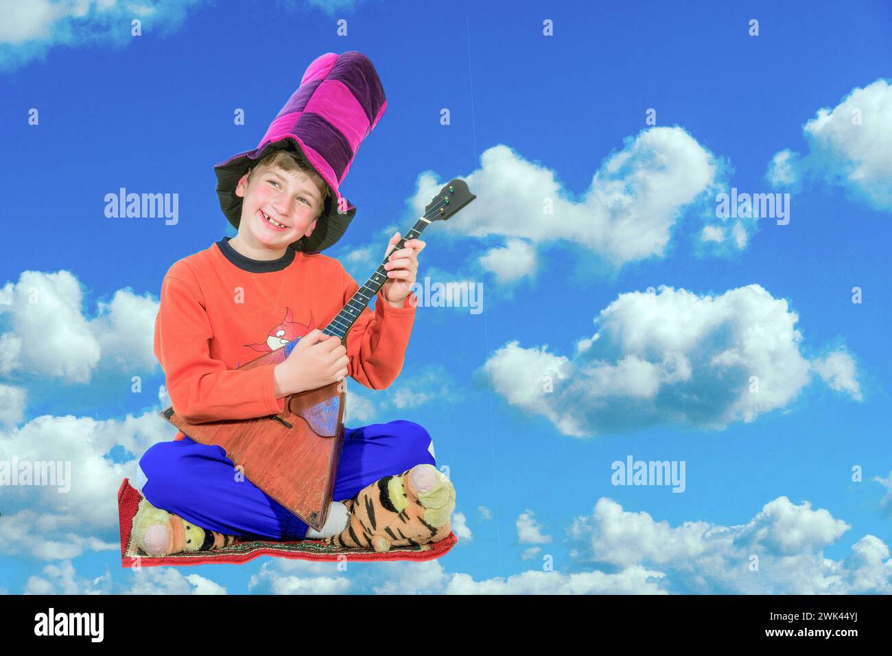 Little Harlequin with a balalaika sits on the carpet and soars in the clouds Stock Photo