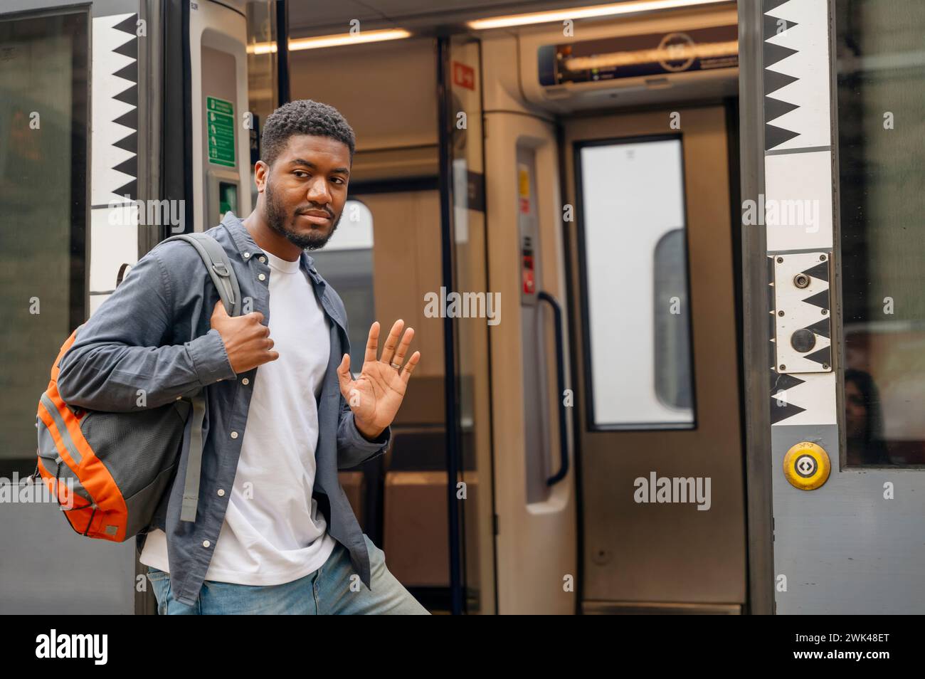 A sad young man getting on a train at the railway station waving goodbye Stock Photo
