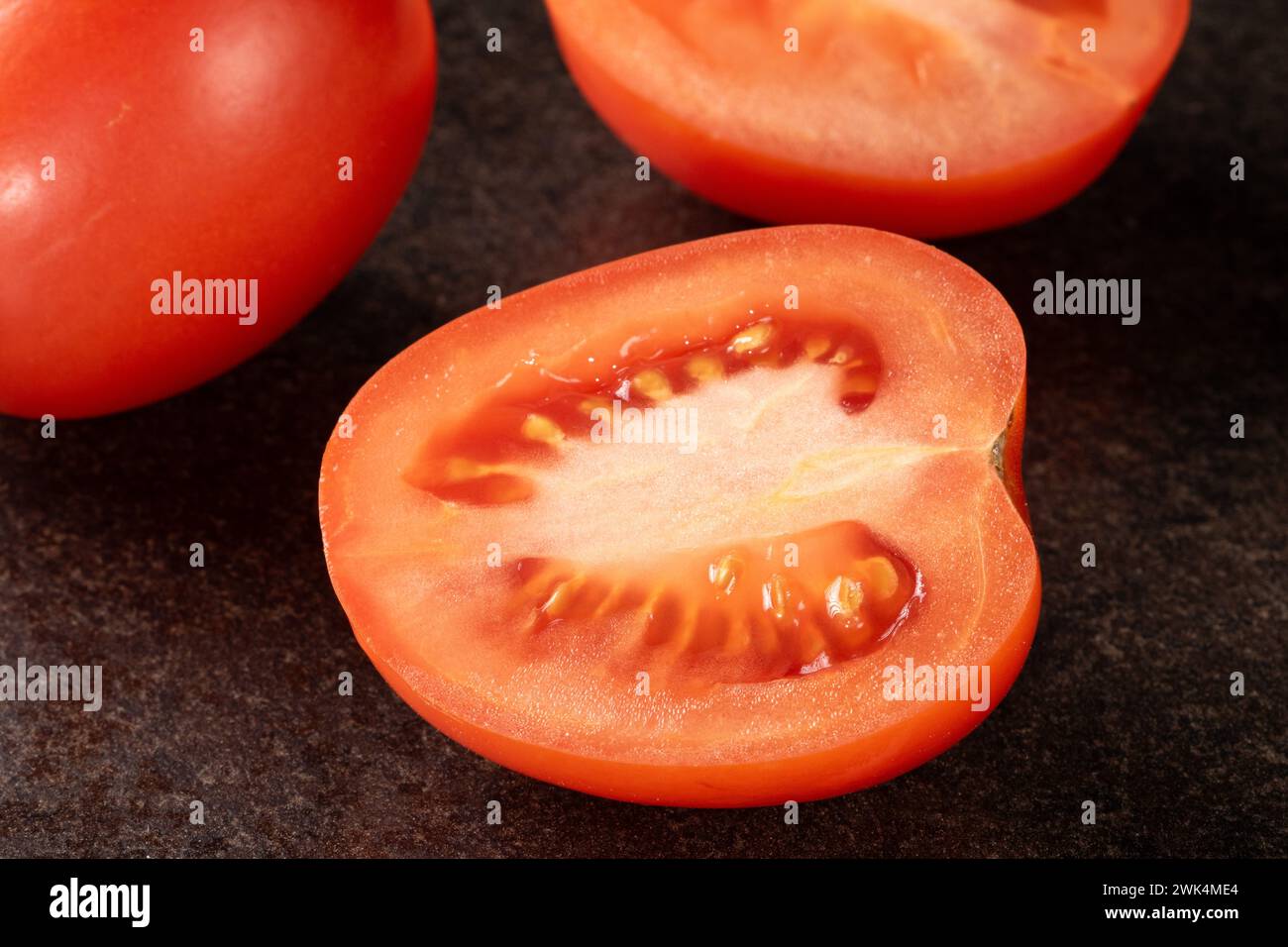 A close-up of a vibrant, freshly sliced tomato, with water droplets glistening on its surface, displayed on a sleek and elegant black background, perf Stock Photo