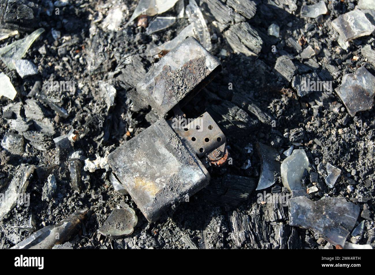 Consequences of the fire. Burnt metal lighter in ashes. Close-up. Stock Photo