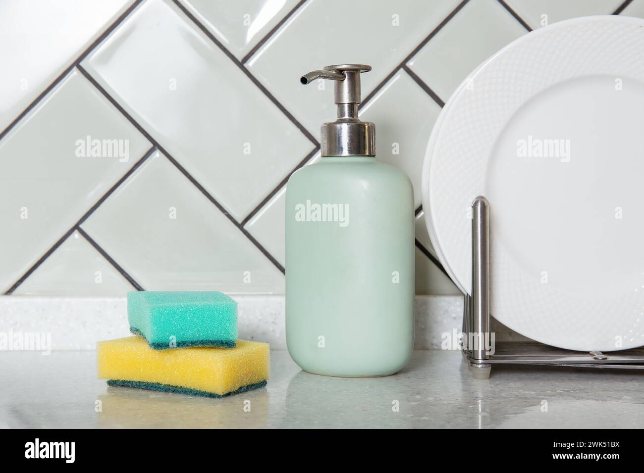 Soap dispenser and sponges beside clean dishes or white plates. Home hygiene and dish washing, home decor Stock Photo