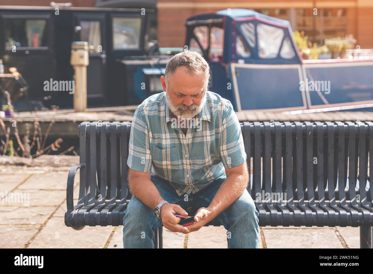 Mature man sitting on a bench and using a smartphone Stock Photo