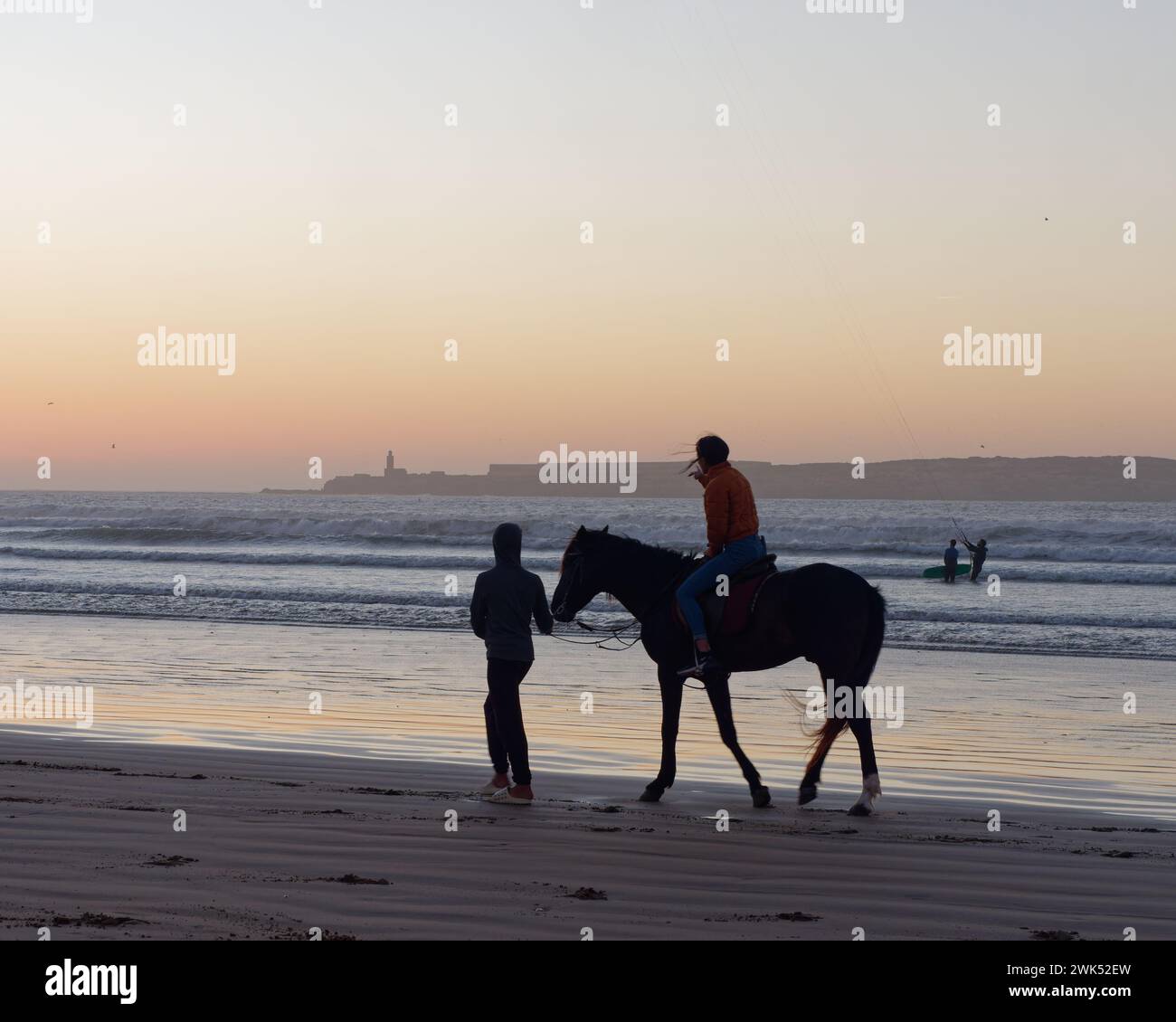 Horse riders being led on a sandy beach at sunset in Essaouira, Morocco. February 18th, 2024 Stock Photo