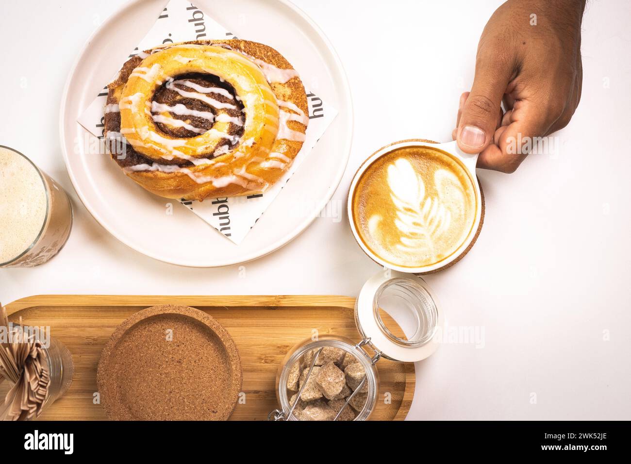 A person is smiling while holding a clear glass cup in one hand and a delicious pastry in the other Stock Photo