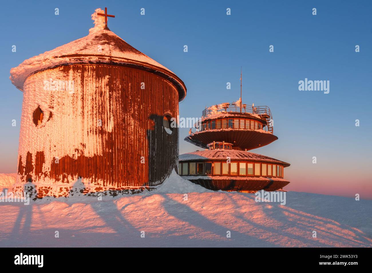 Winter, sunrise time, wooden Roman catholic chapel and disc shaped meteorological observatory in snezka, mountain on the border between Czech Republic Stock Photo