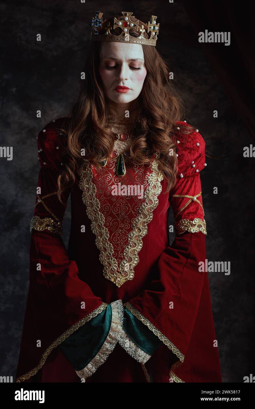 medieval queen in red dress with white makeup and crown on dark gray ...