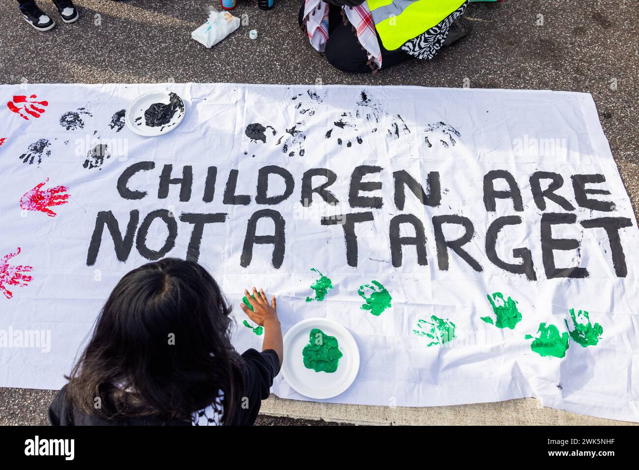 Wakefield, UK. 18 FEB, 2024. Child adds handprint onto banner reading 'Children are not a target' at the begining of Wakefields first pro palestine march. Credit Milo Chandler/Alamy Live News Stock Photo