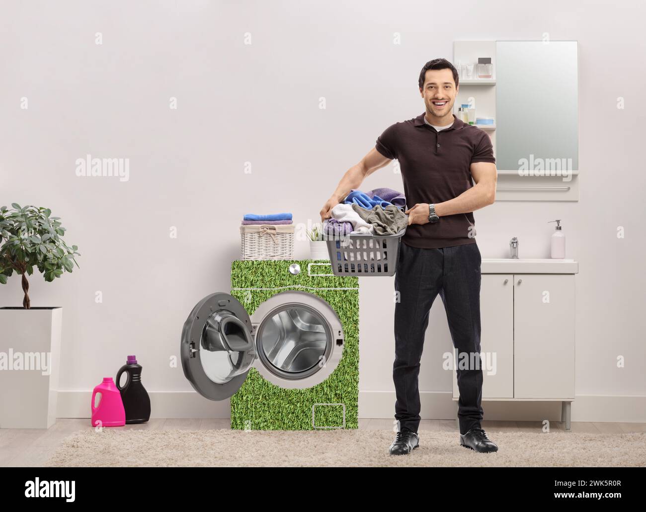 Young man with a laundry basket full of clothes standing in a bathroom next to energy efficient washing machine Stock Photo