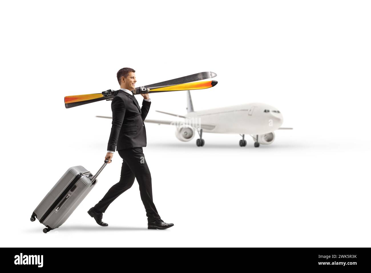 Full length profile shot of a businessman carrying skiis and pulling a suitcase in front of a plane isolated on a white background Stock Photo